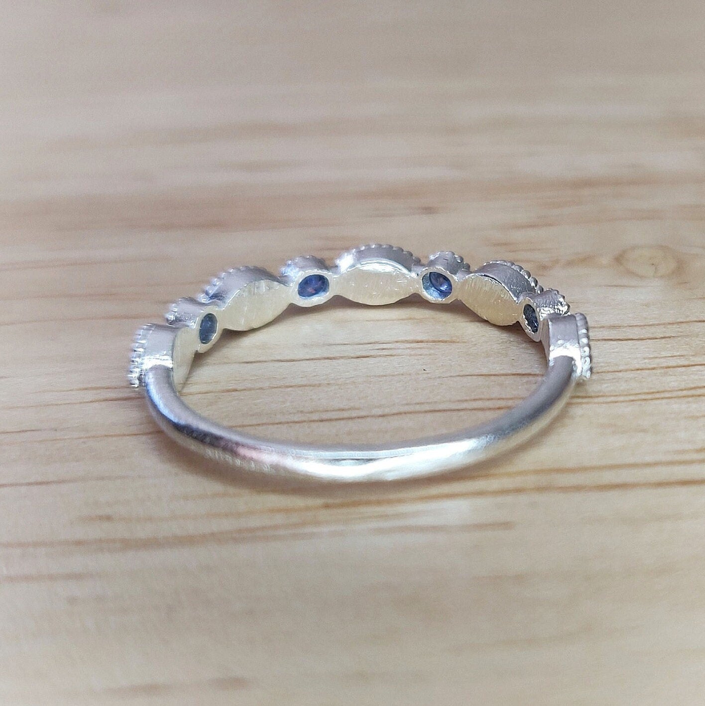rear view of a silver eternity stacking ring with blue sapphires on a wooden table.