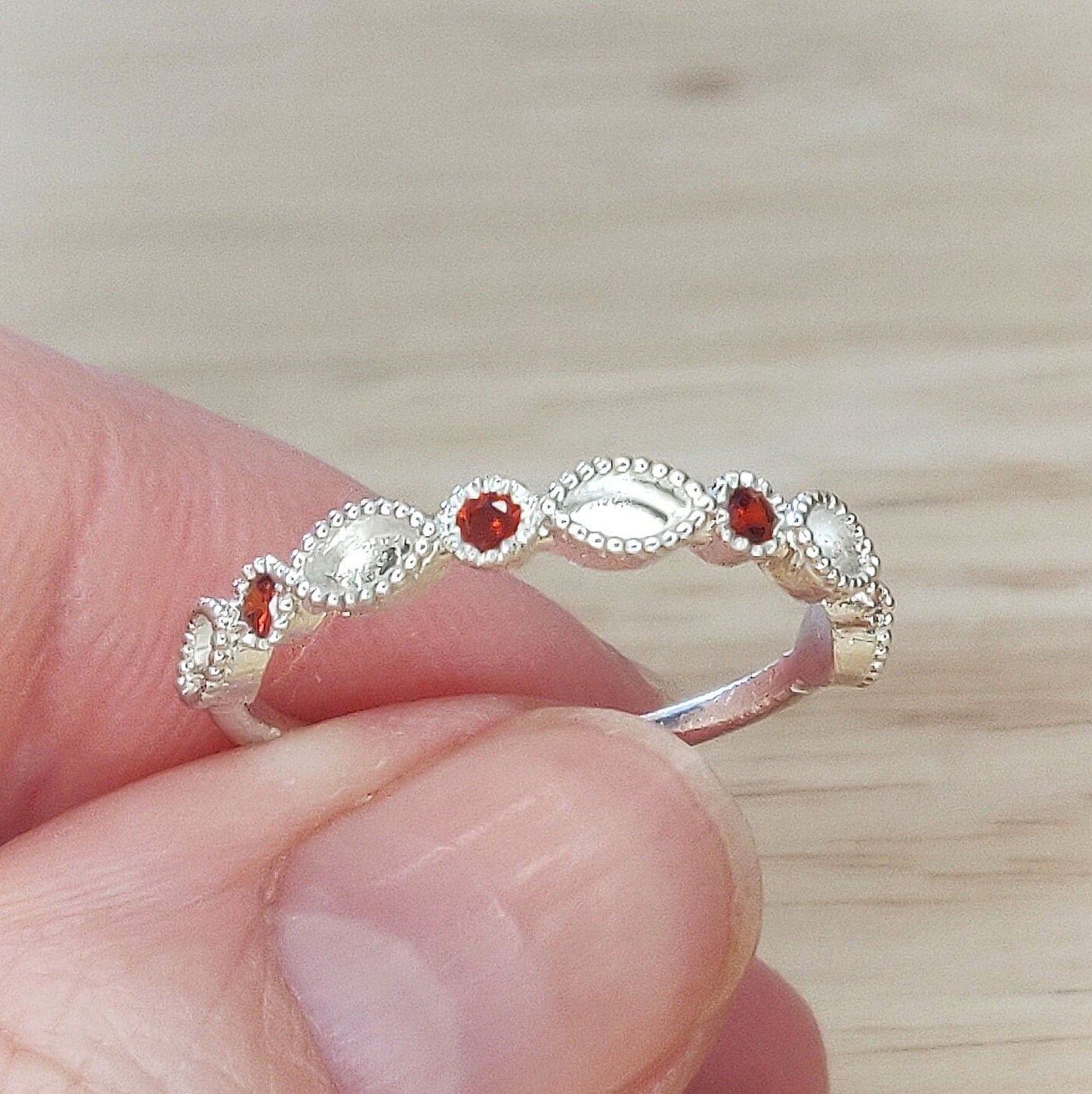 Image of ruby birthstone eternity ring being held between two fingers.