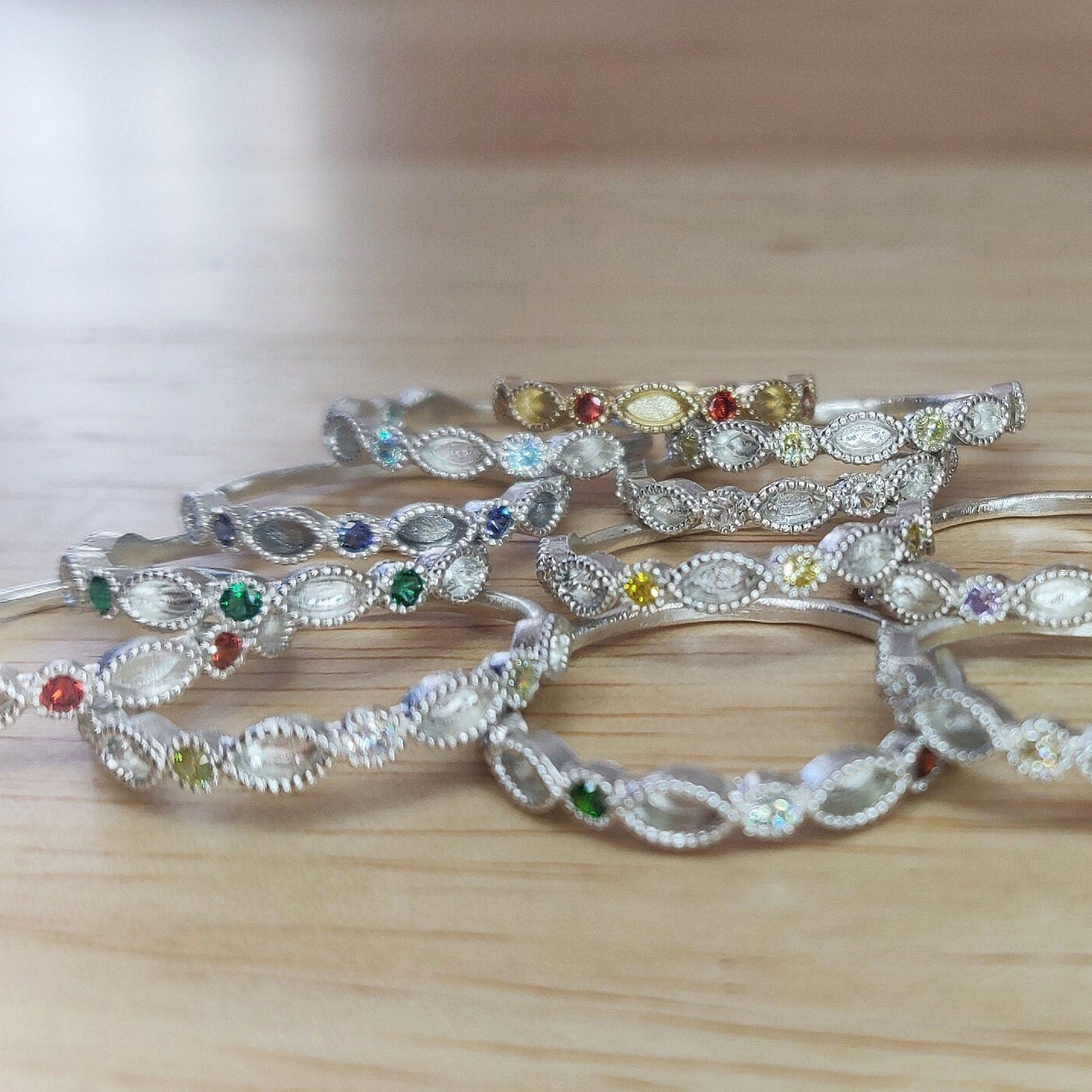 Selection of marquise and round cut eternity rings with different birthstones on a wooden background.