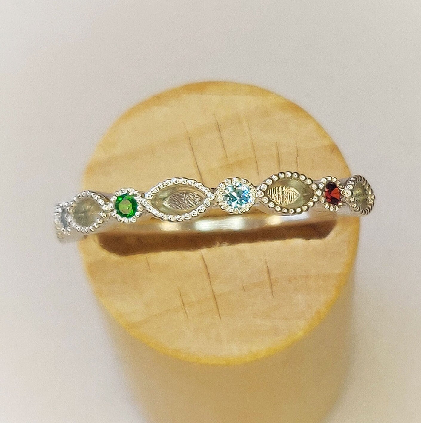 Birthstone silver eternity ring in a wooden stand.