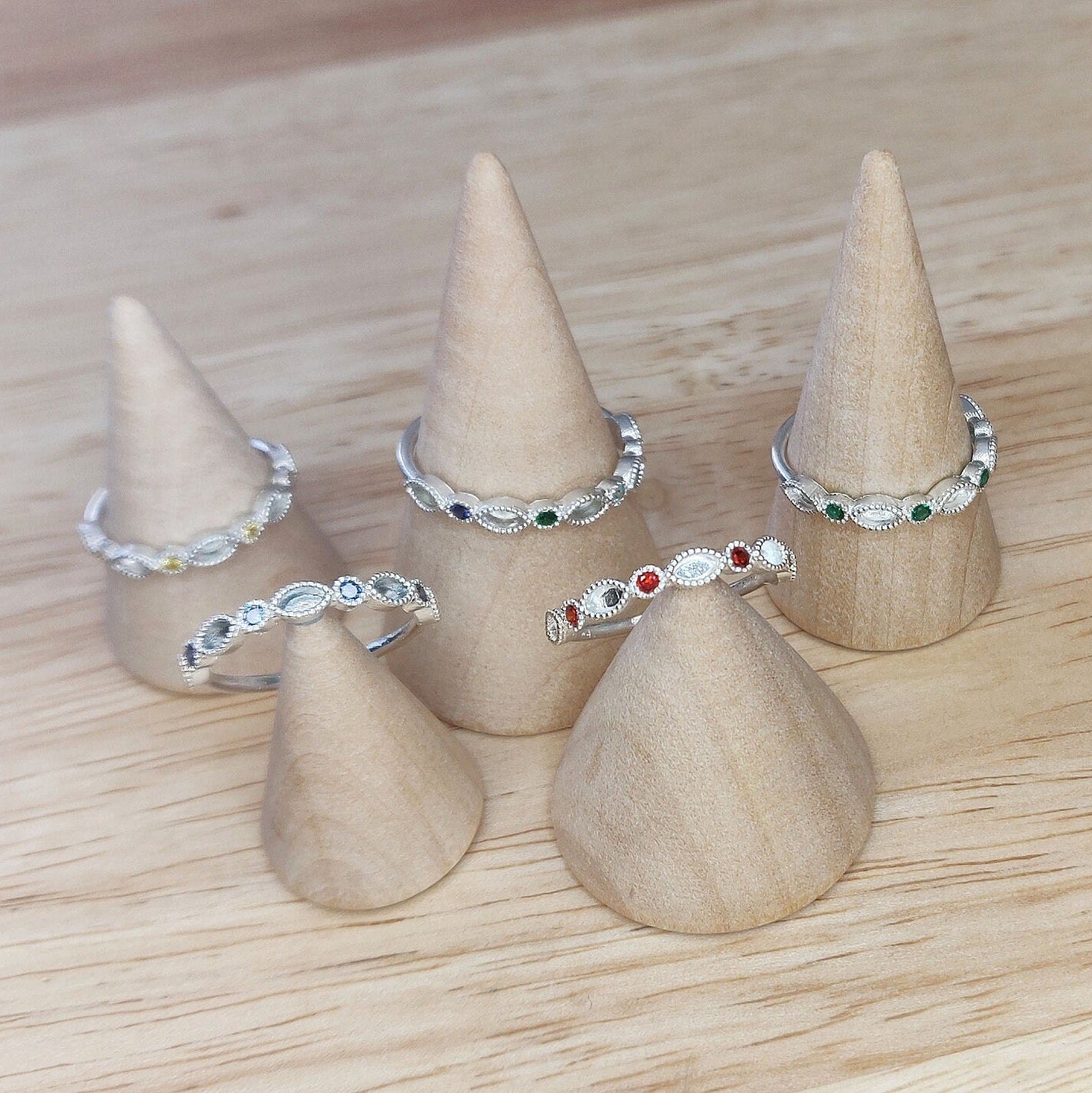 Selection of minimalist eternity rings with birthstones on wooden cones for display.