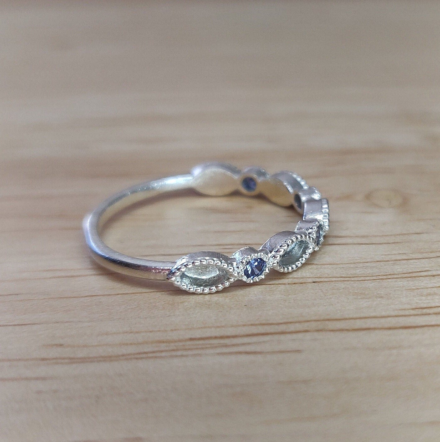 Side view of a silver eternity stacking ring with blue sapphires on a wooden table.