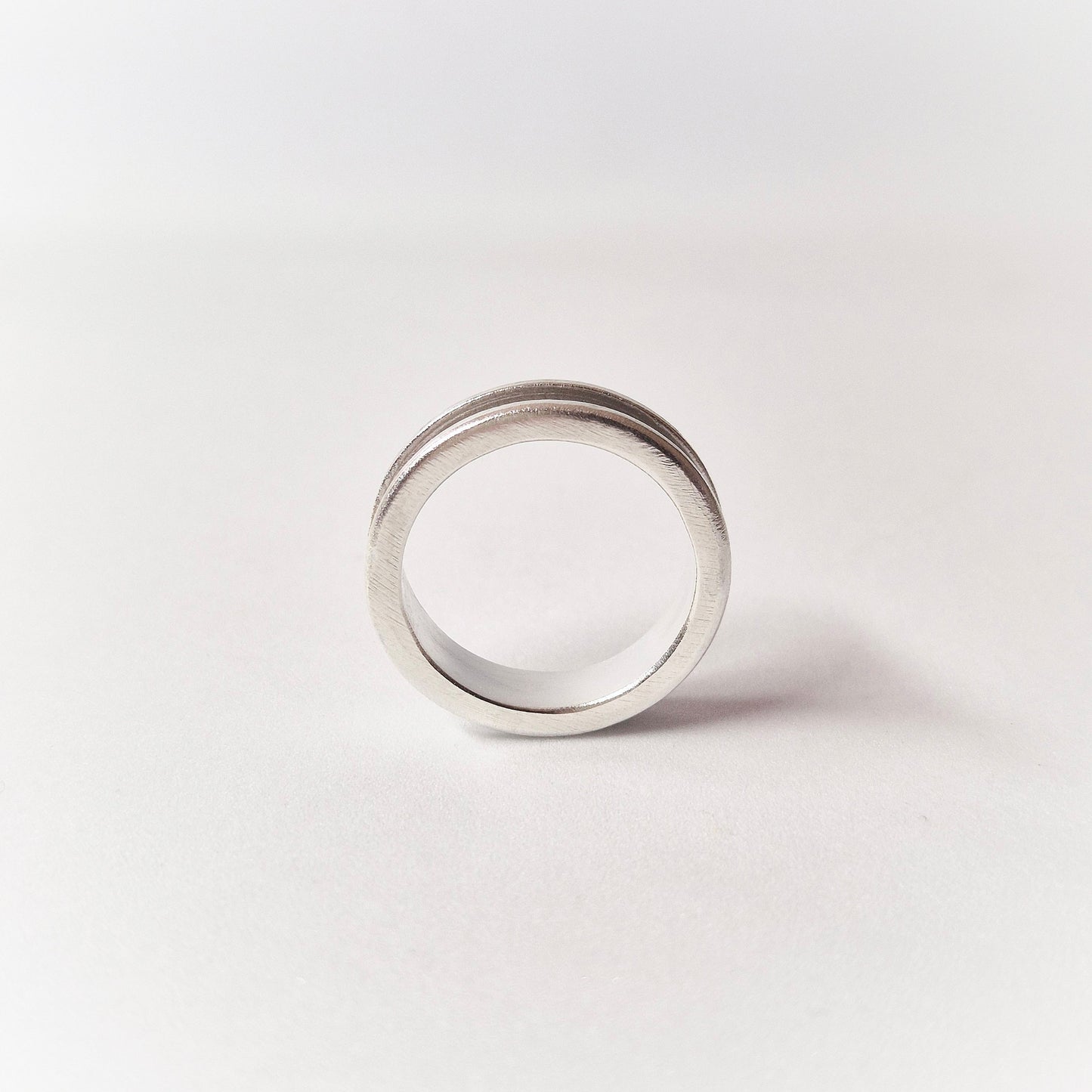 Through Finger View of a Silver Channel Ring on a White Background.