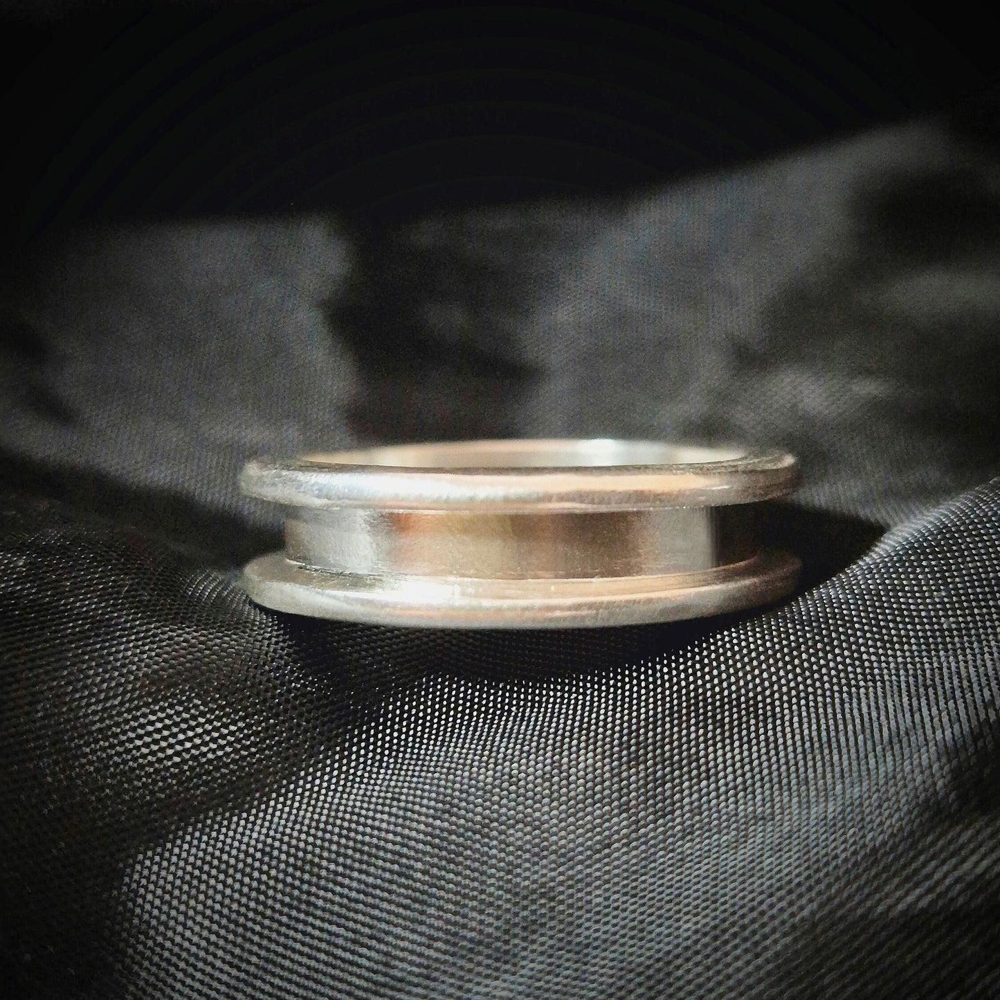 Silver Channel Ring sitting flat on black material background