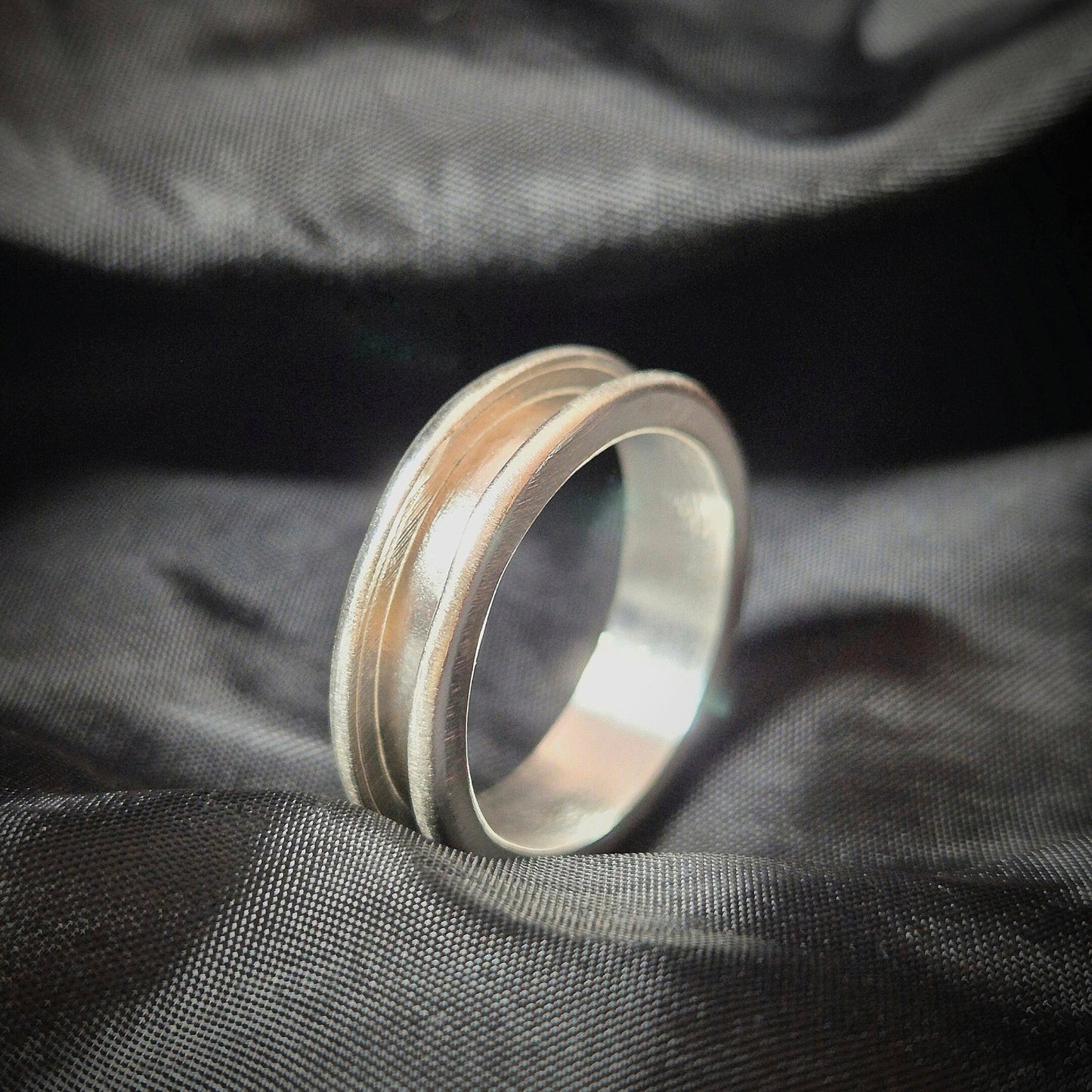 Profile View of Silver Channel Ring on a Black Material Background.