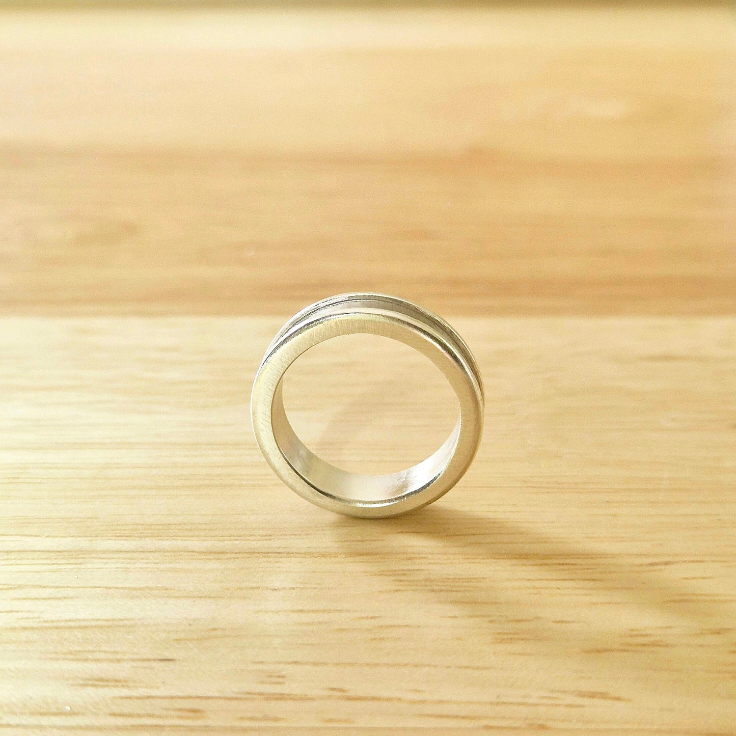 Through Finger View of a Silver Channel Ring on a Wooden Background.