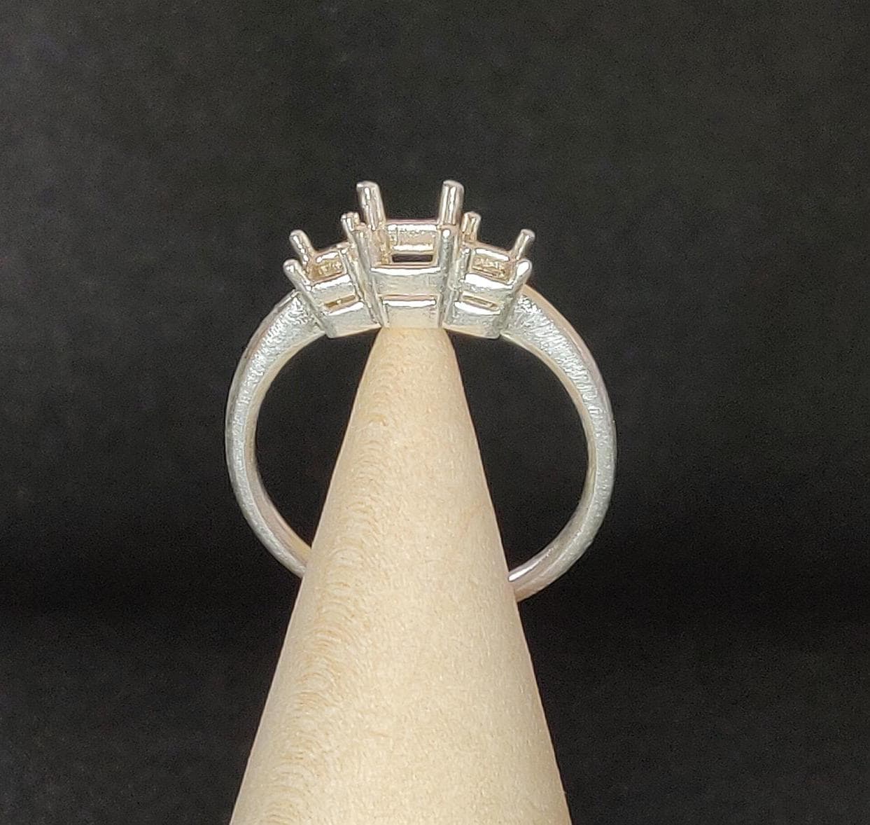 Wooden cone balancing a silver 3 stone ring for princess stones.