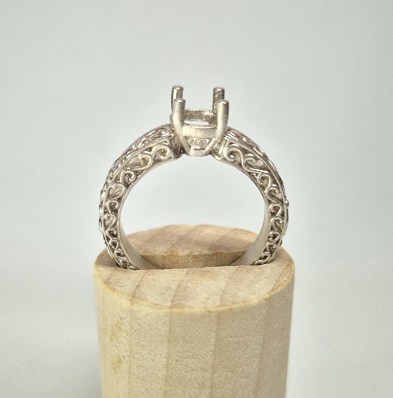 Silver scroll ring with intricate patterns in a display stand.