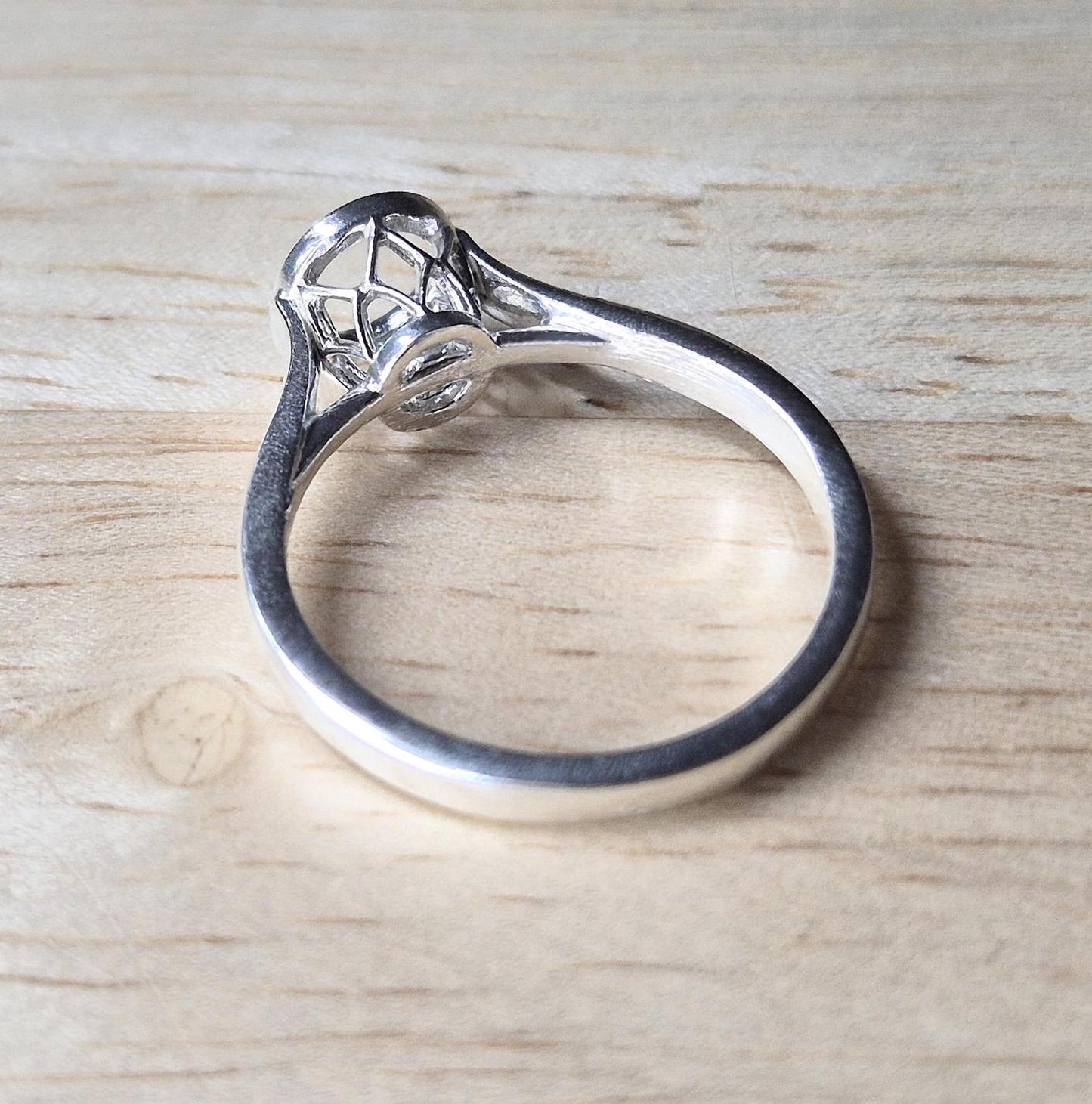 Silver cathedral shank ring with basket bezel on a wooden background.