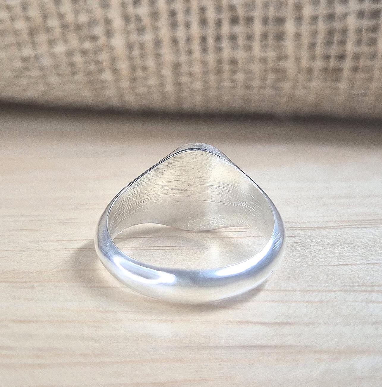 Rear view of an oval silver signet ring on a desk.