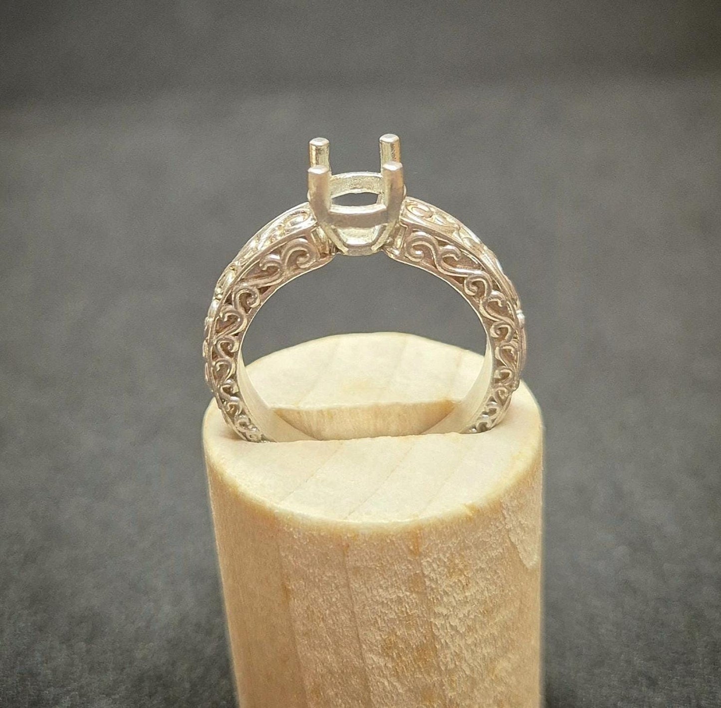 Wooden display with a silver antique victorian styled ring for gem setting.