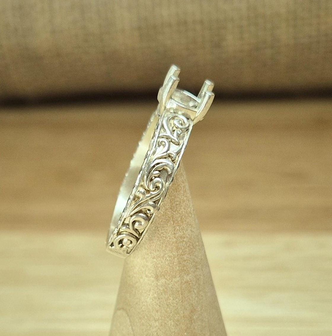 Side view of the scroll design on a silver engagement style ring for gem setting.