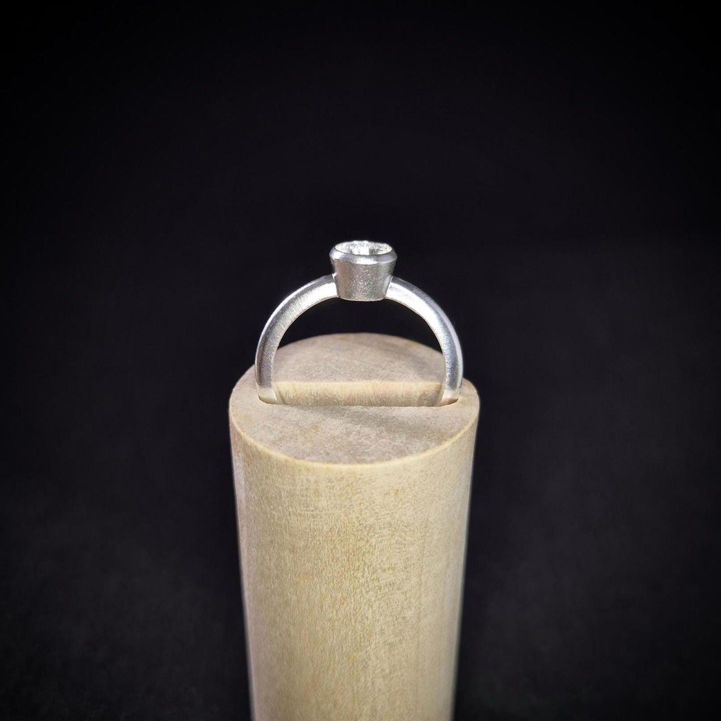 Empty Silver Bezel Ring in a Wooden Stand Against a Black Background.