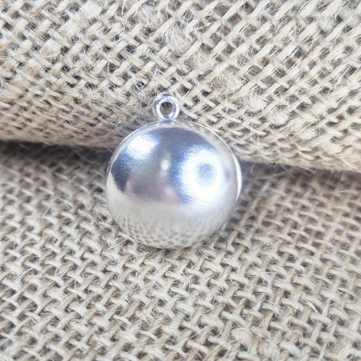 Front View of a Round Silver Locket against a Jute Background.
