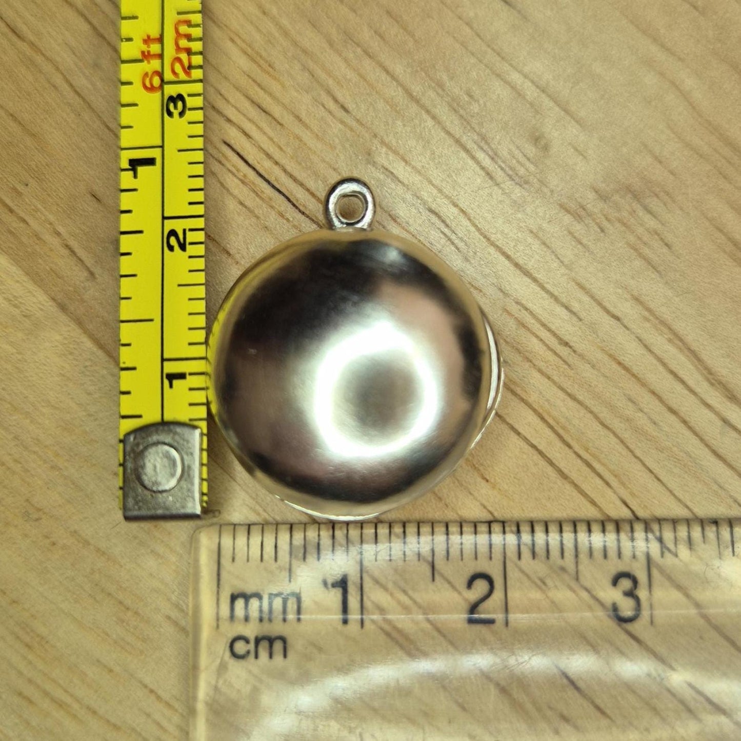 Closed Round Silver Locket with Measuring Tape and Ruler for Scale.