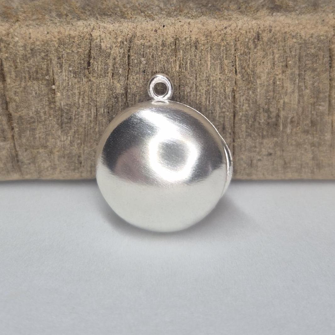 Closed Round Silver Locket Standing Against a Wooden Block.