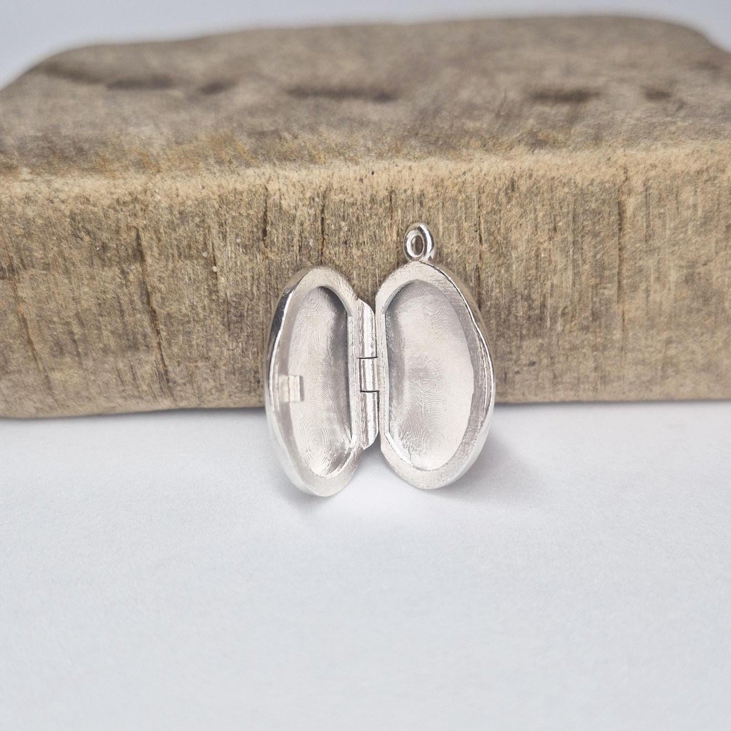 Open Oval Silver Locket Standing By a Wooden Block.
