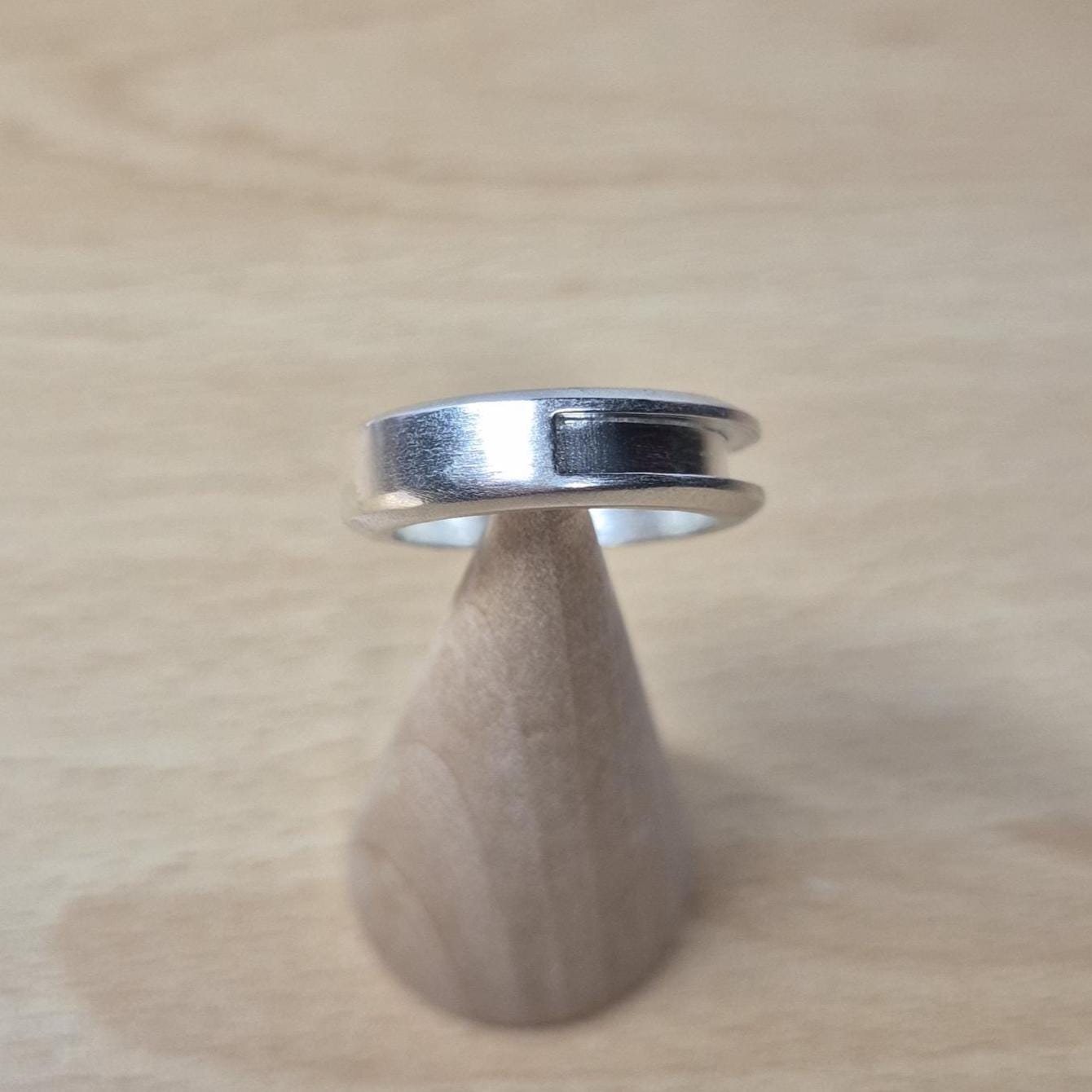 Blank silver half channel ring displayed upright on a wooden ring cone, with soft lighting emphasizing its clean edge and unfinished surface.