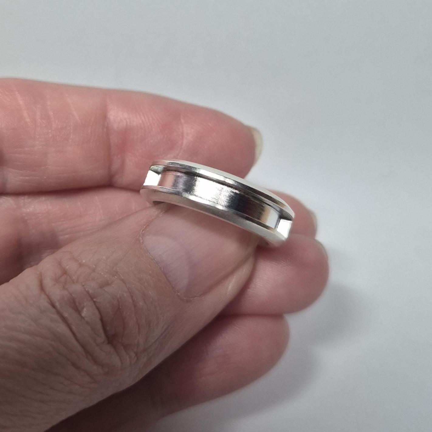 Half channel silver ring held gently in hand, emphasizing the clean, symmetrical groove suitable for stone setting.