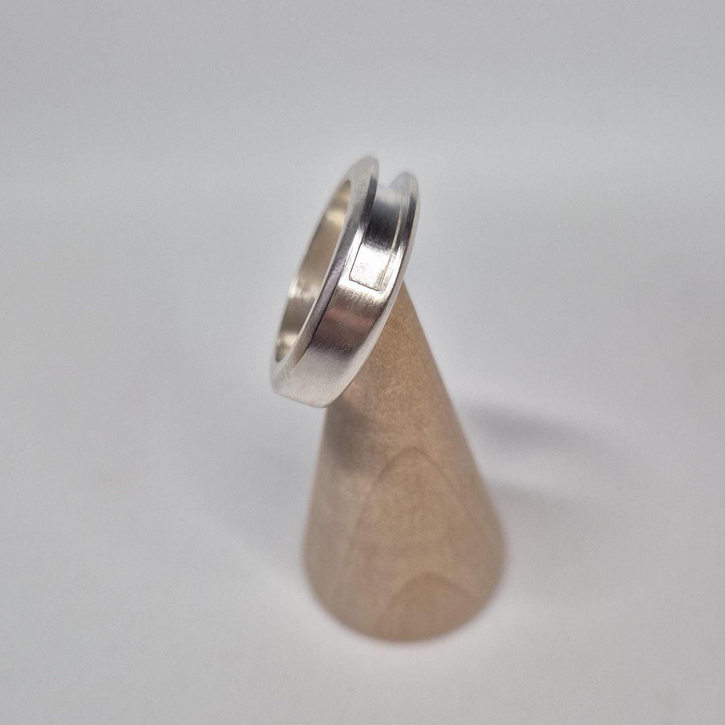 Half channel ring displayed upright on a wooden mandrel cone, with the grooved design clearly visible along the side.