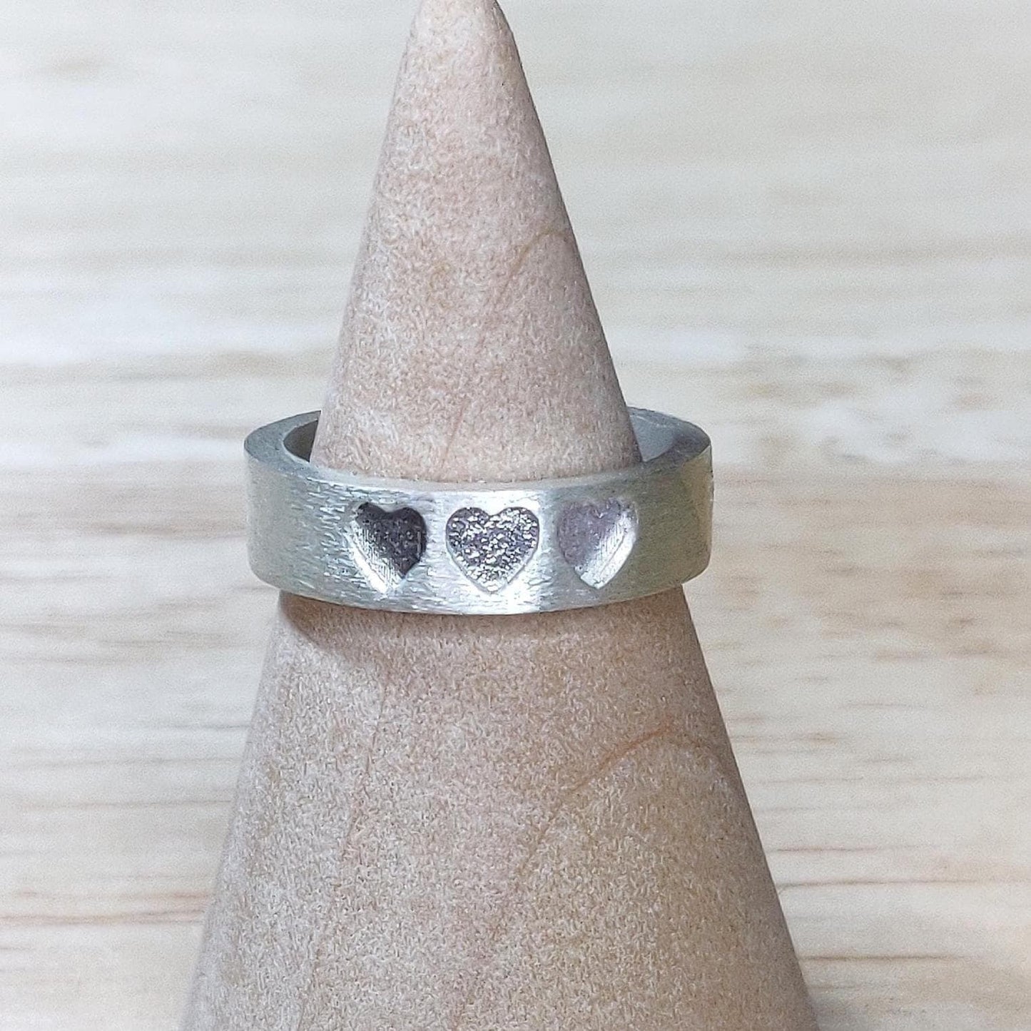 Three-heart silver ring displayed on a wooden ring cone, ideal for ashes or breastmilk resin fillings.