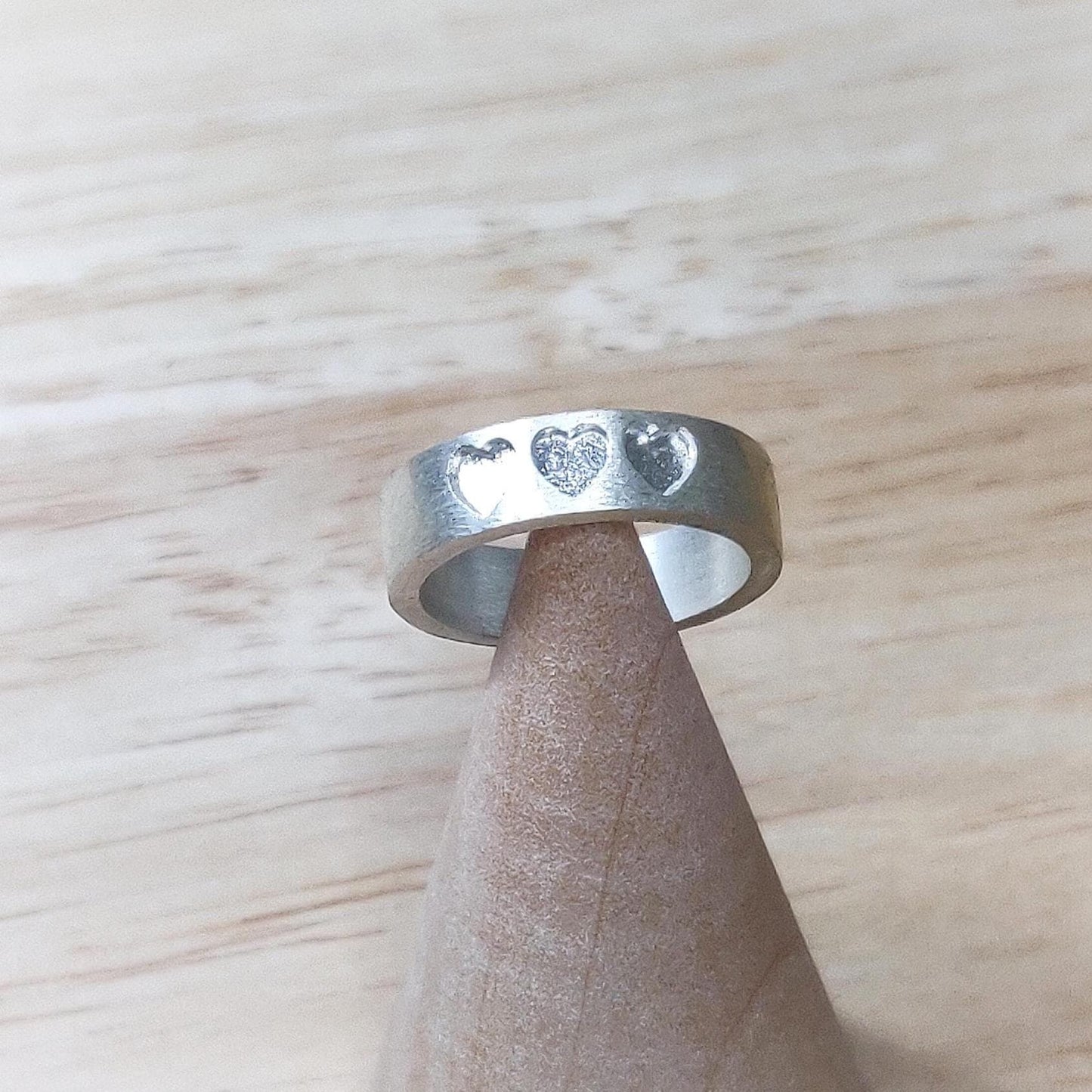 Artisan silver band with recessed hearts on a cone stand, set against a light wood backdrop.