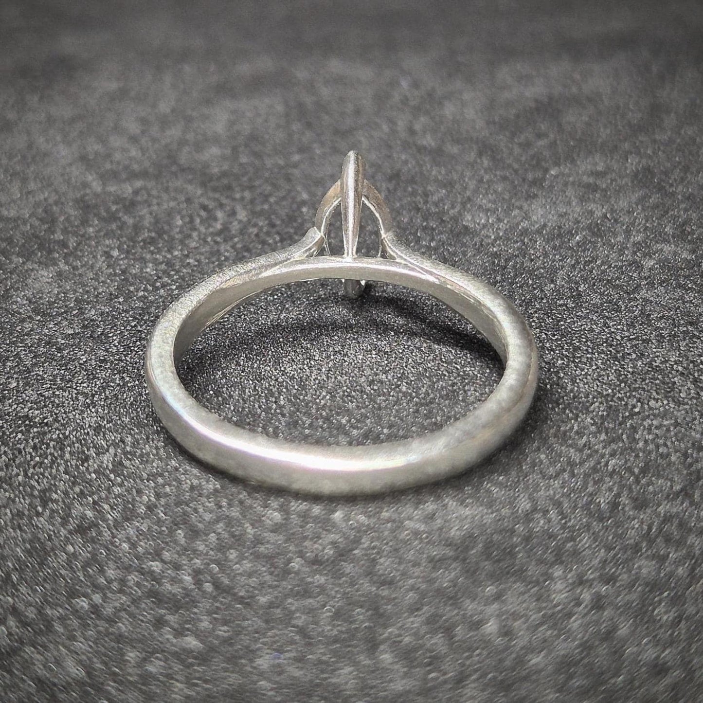 Rear view of a silver ring blank with raised cathedral shoulders and an empty marquise setting, displayed on a dark surface.