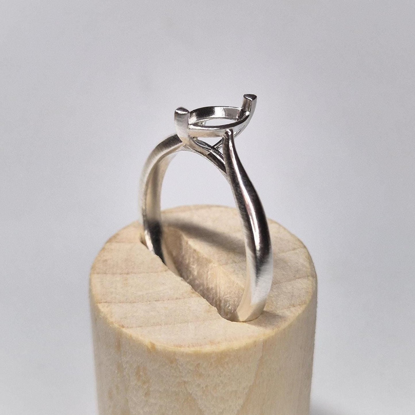 Side profile of a cathedral shank silver ring blank with a 2-prong marquise setting, displayed on a round wooden base.