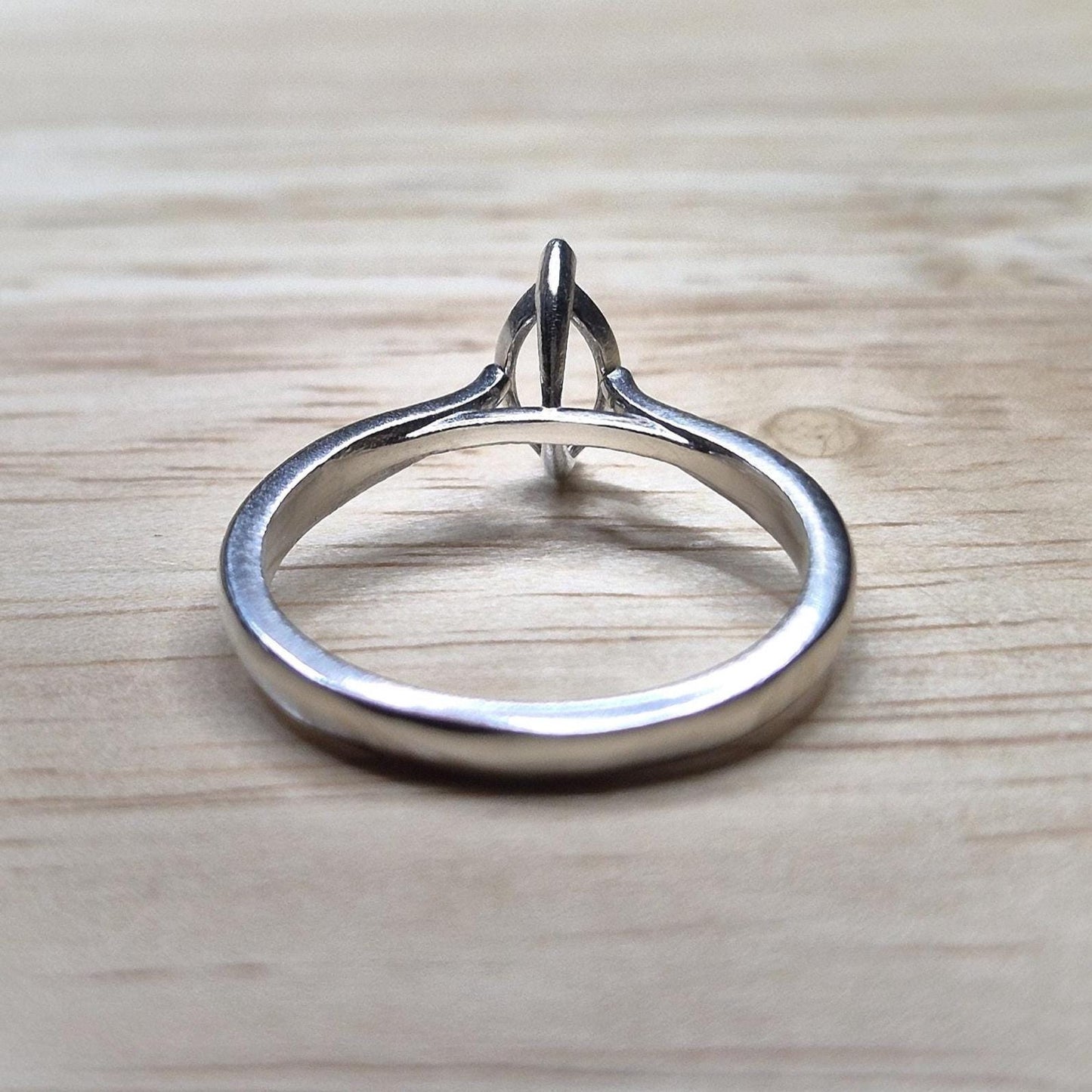 Flat lay of a silver cathedral shank ring blank with an empty 2-prong marquise setting, displayed on a light wooden surface.