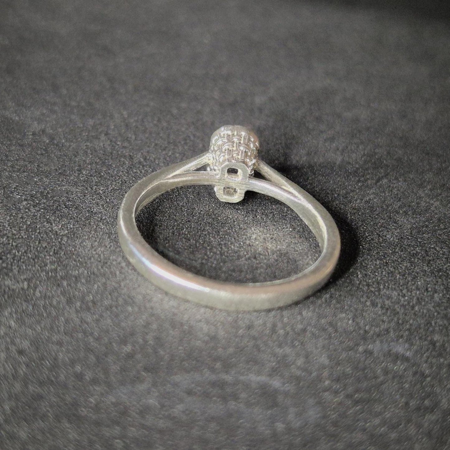 Silver ring blank with a cathedral shank and basket bezel setting for an emerald cut stone, shown from the rear on a dark background.