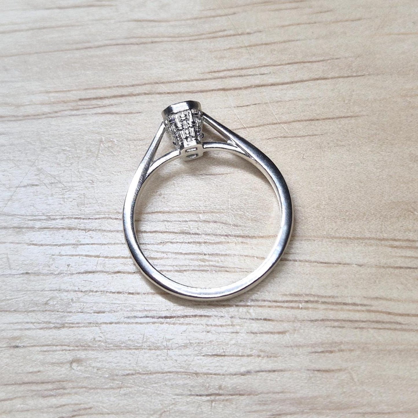 Flat lay of an unset emerald-cut ring blank with open basket design, shown on a pale wood surface.