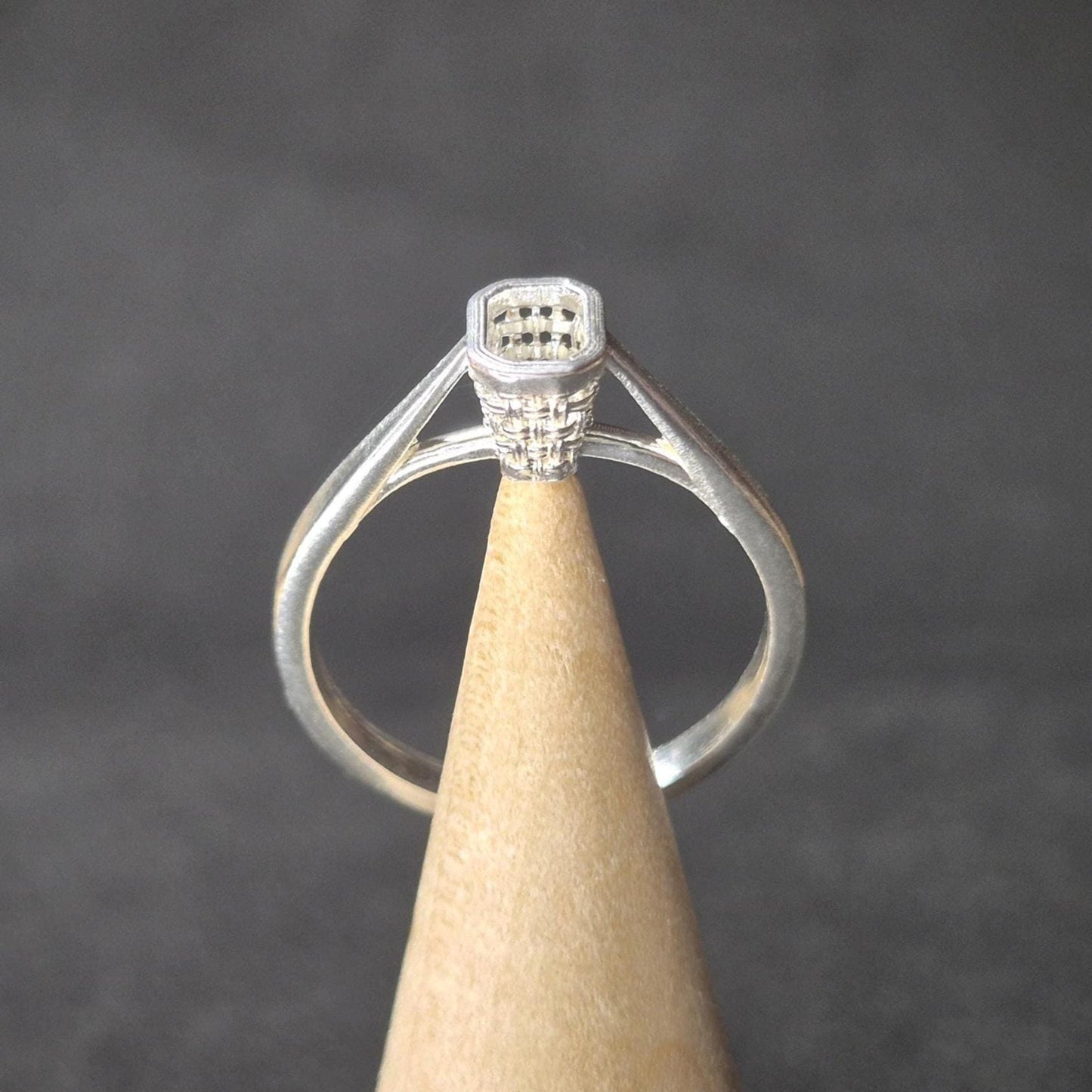 Front view of a silver emerald-cut ring blank on a wooden cone, shown against a dark background for contrast.