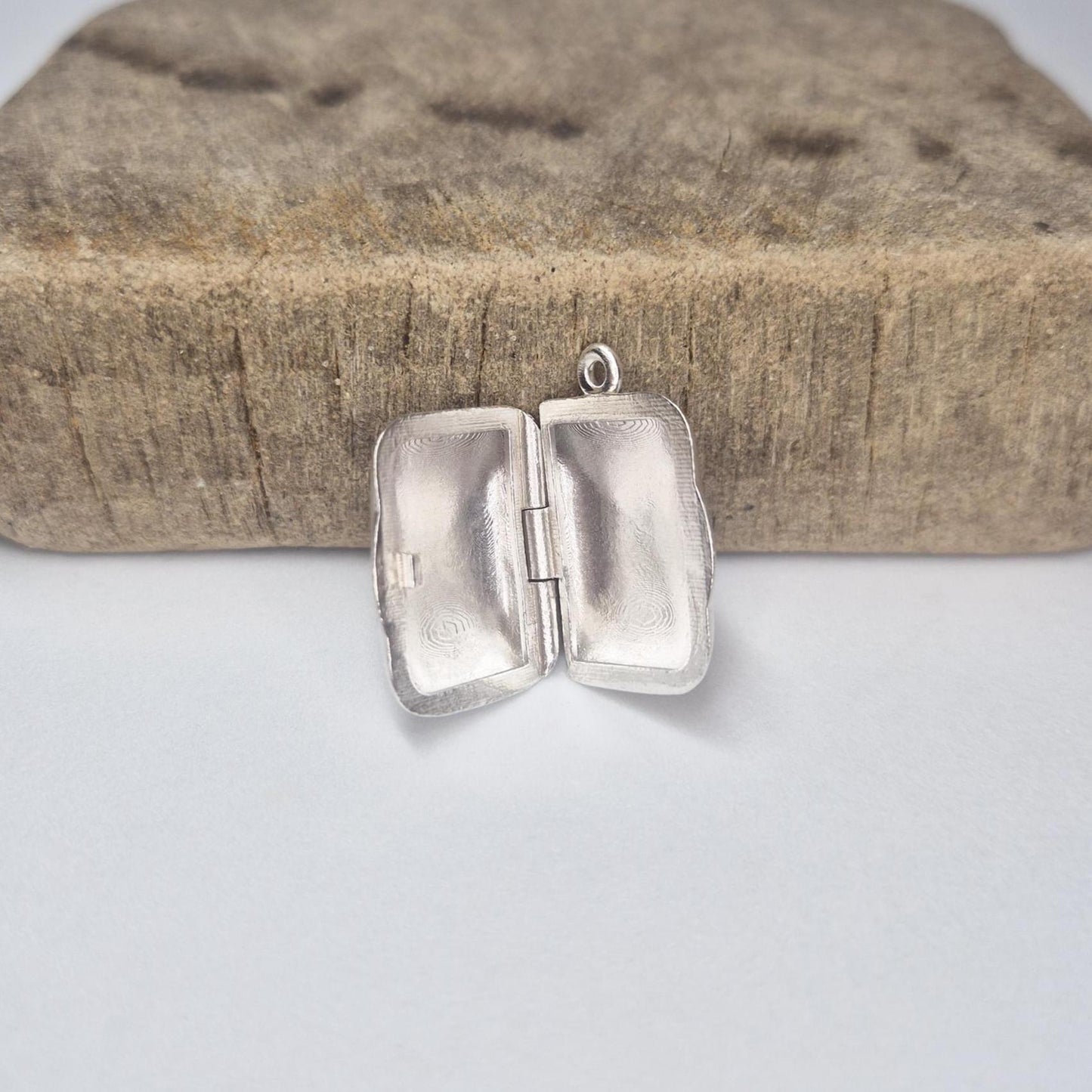 Rectangular silver locket opened on a wood block, highlighting inside surfaces and handcrafted details.