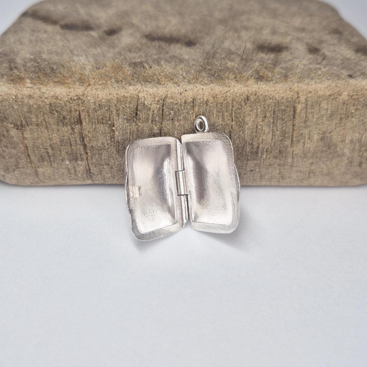 Rectangular silver locket opened on a wood block, highlighting inside surfaces and handcrafted details.