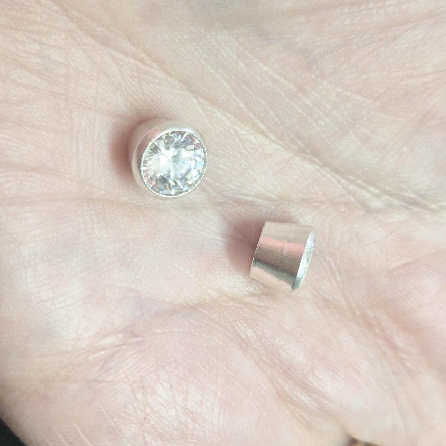 7mm round brilliant-cut gemstone set in sterling silver bezel setting, shown alongside an empty rubover cup in hand