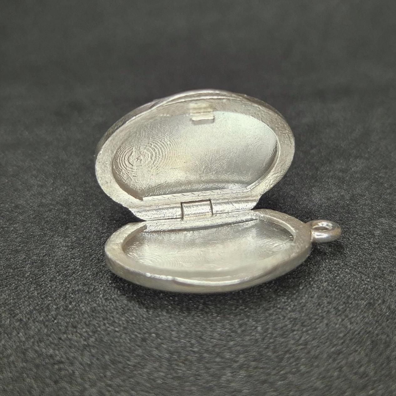 Open Oval Silver Locket on Its Side Against a Black Background.