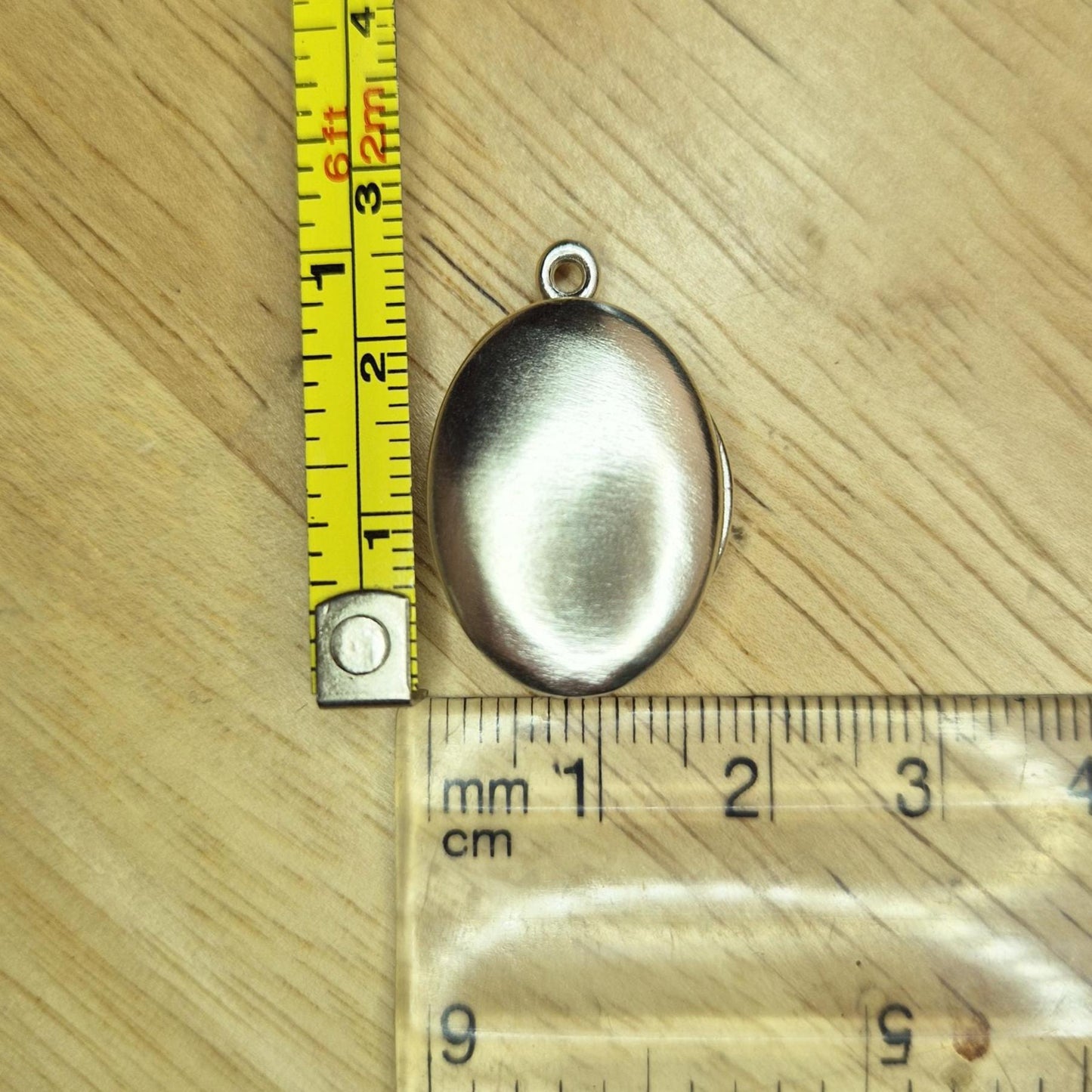 Oval Silver Locket With a Measuring Tape and Ruler for Scale.