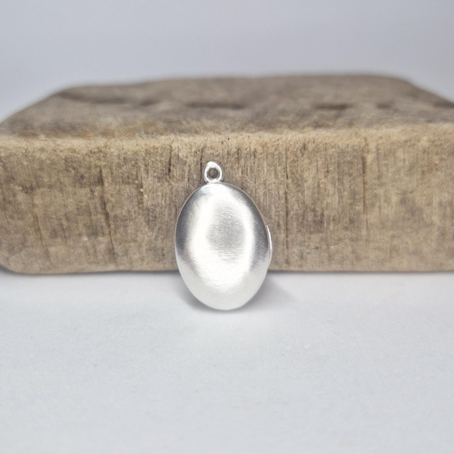 Closed Oval Silver Locket Standing Against a Wooden Block.