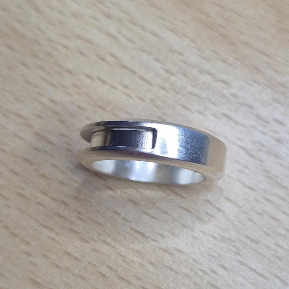 Minimalist silver half channel ring lying on a light wood surface, viewed at an angle to show its brushed finish and inset groove.