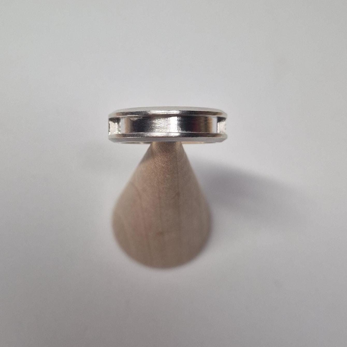 Oblique view of a half channel silver ring on a wooden cone, showing the recessed channel cut into the outer band.