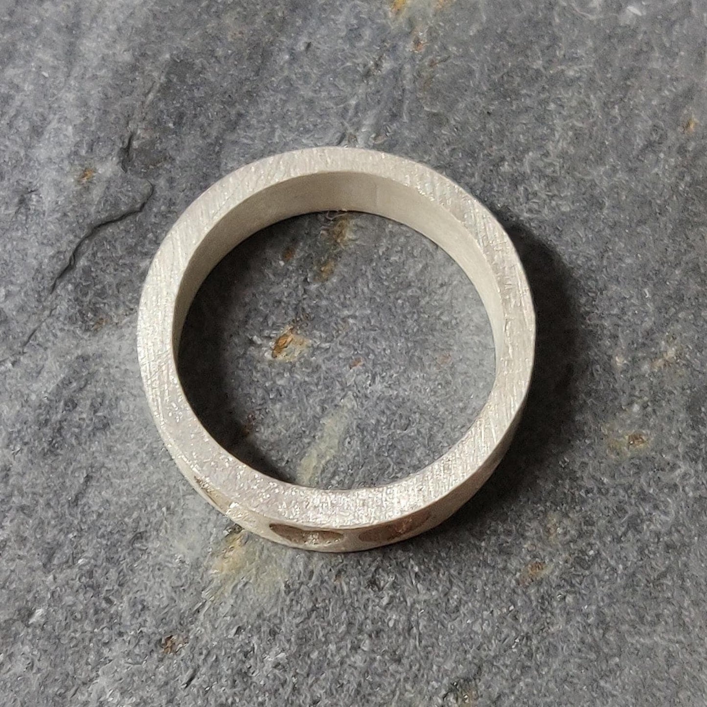 Top view of a silver keepsake ring featuring three heart-shaped recesses, placed on a natural stone surface.