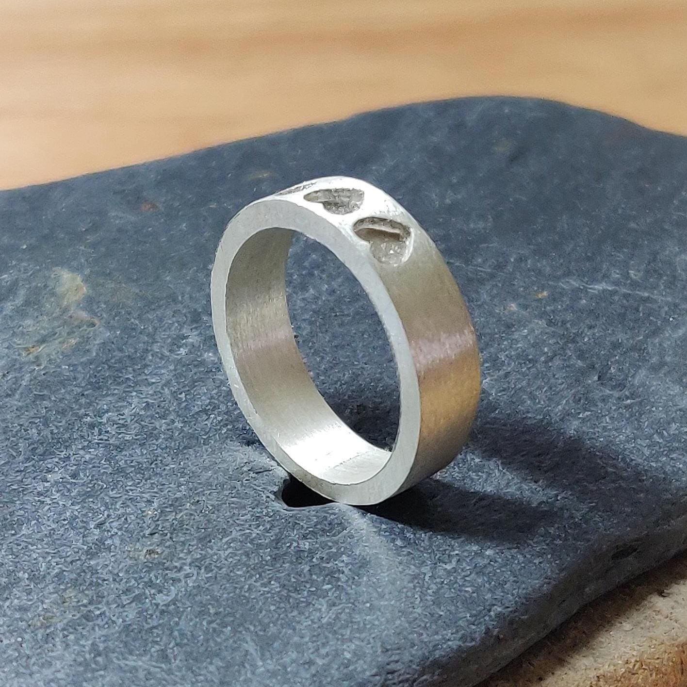 Angled view of a silver cremation or breastmilk ring with three recessed hearts, resting on slate.