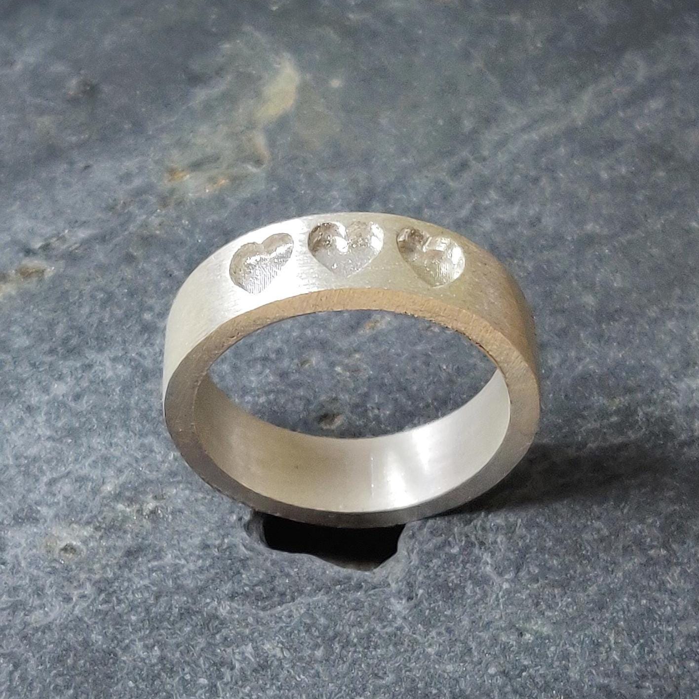 Side profile of a handmade silver memorial ring, highlighting the depth of the three recessed heart shapes.