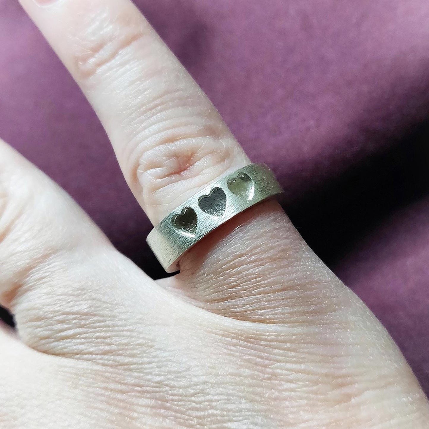 Silver ring with recessed hearts shown upright, emphasizing the smooth interior and textured exterior.
