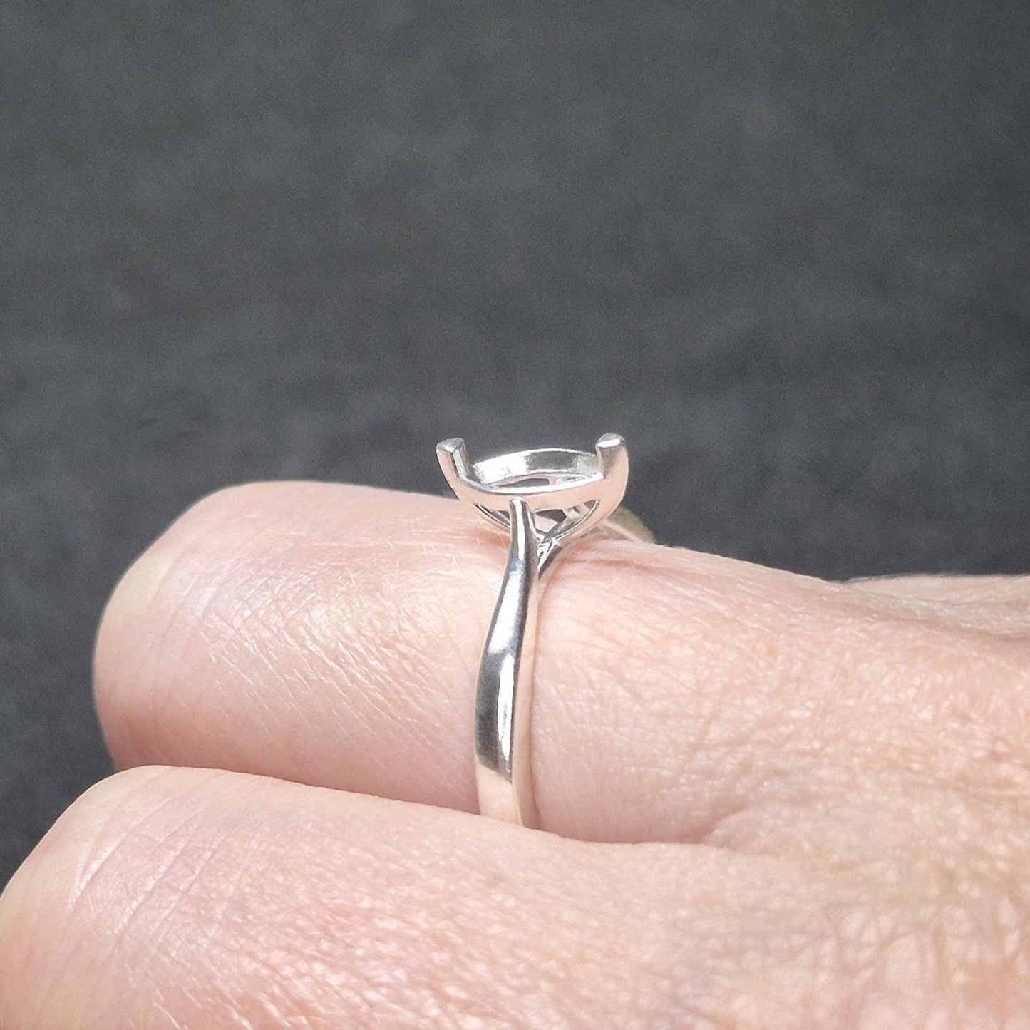 Sterling silver ring blank with a cathedral shank and 2-prong marquise setting, shown on a finger against a dark background.
