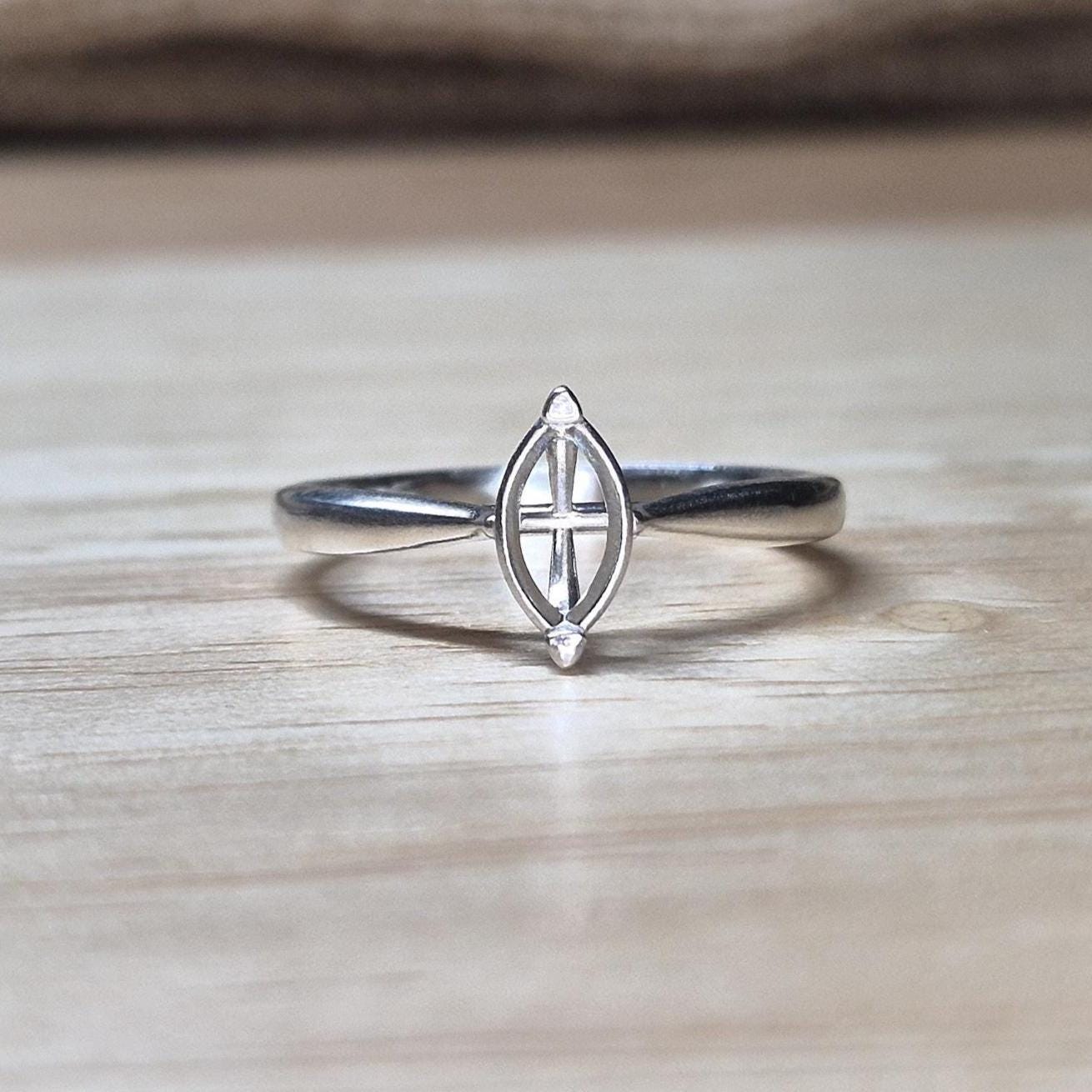 Front-facing shot of a silver ring blank with marquise prongs, ideal for an 8x4mm stone, on a wood backdrop with neutral tones.