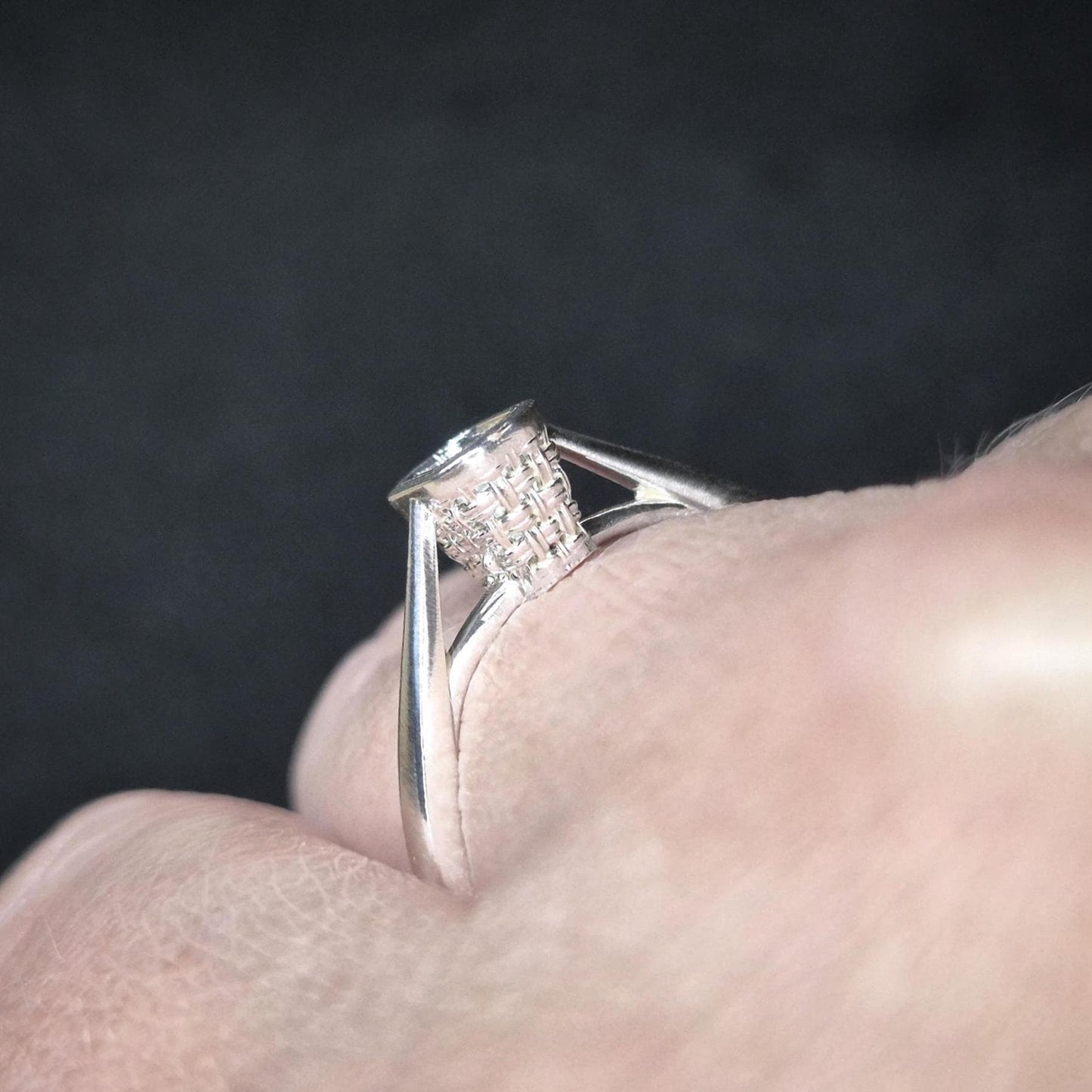 Close-up of a silver ring with basket bezel setting on a finger, highlighting the cathedral shank design.