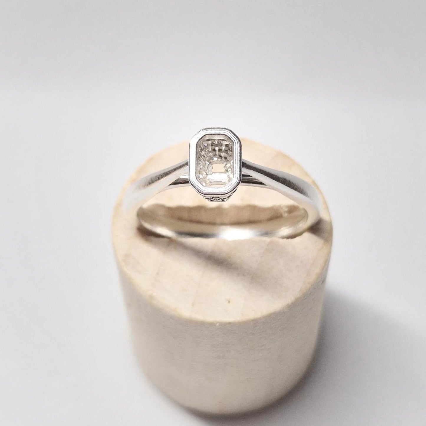 Front view of the basket bezel ring blank on a wooden block, showing the rectangular emerald-shaped opening from above.