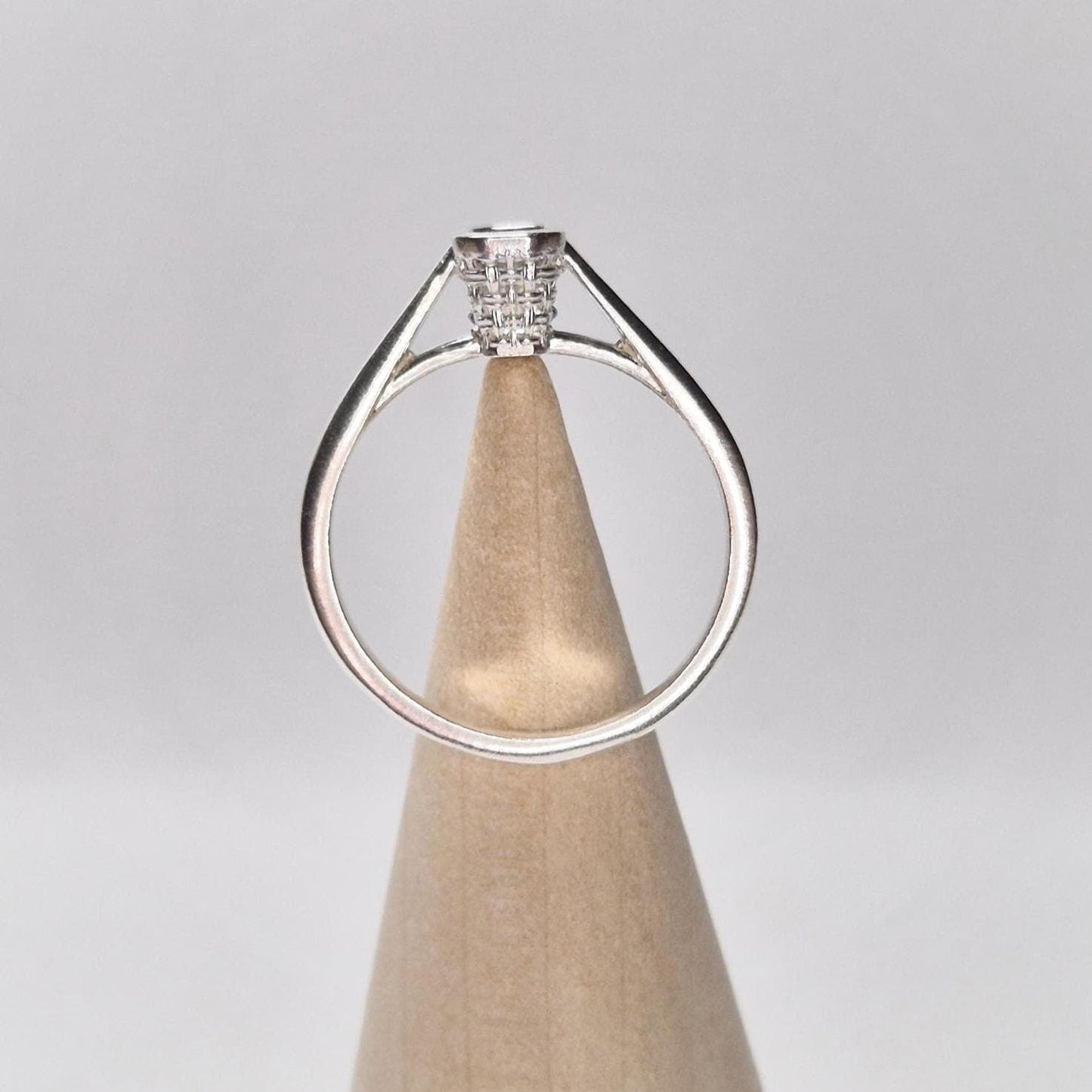 Side view of silver basket bezel ring displayed on a wood cone stand, with open cathedral-style shoulders and high-profile setting.