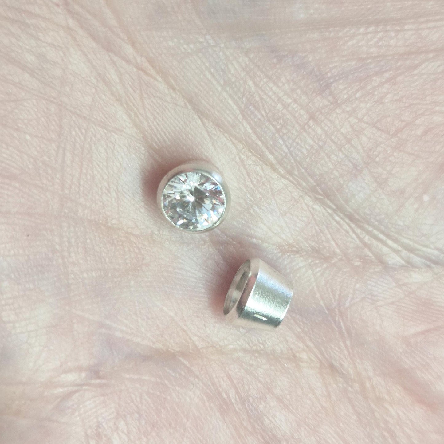 6mm round brilliant-cut gemstone set in sterling silver bezel setting, shown alongside an empty rubover cup in hand